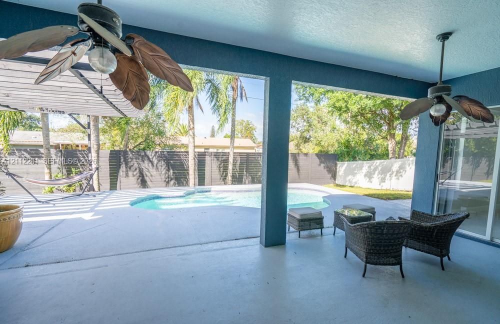 Covered patio featuring two ceiling fans, painted concrete flooring, and an in-ground swimming pool with a privacy fence
