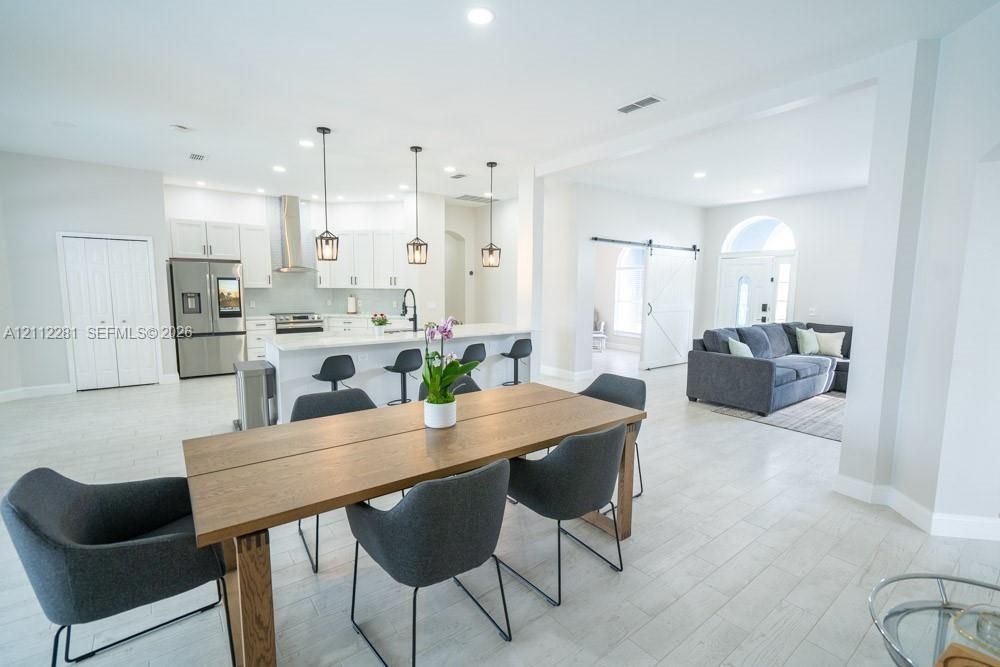 Open-concept space featuring light wood-finish flooring, a kitchen island with stone-style countertops, shaker-style cabinetry, recessed lighting, and a barn-style sliding door