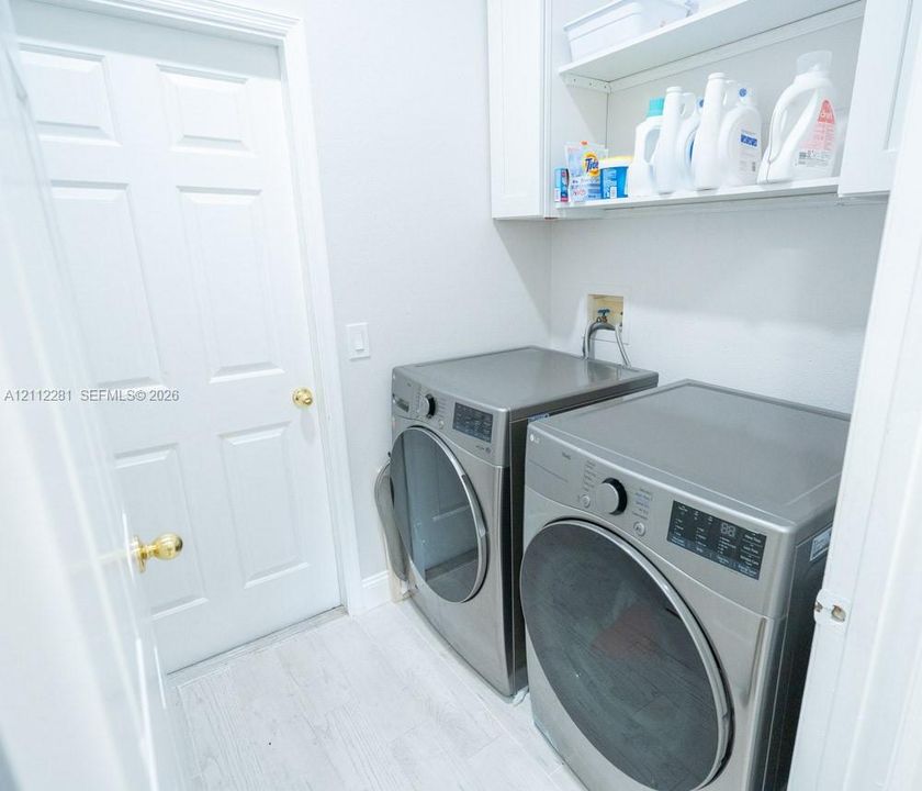 Dedicated utility space featuring white built-in cabinetry, upper shelving, and white tile flooring