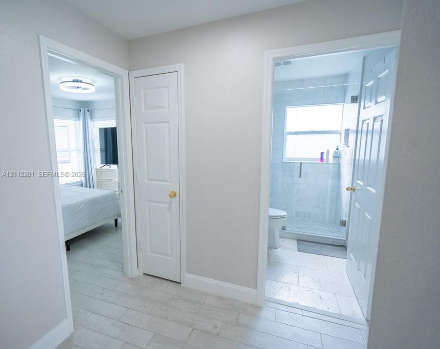 Hallway featuring wood-finish flooring, white panel doors, and entry into a bathroom with tile surround shower