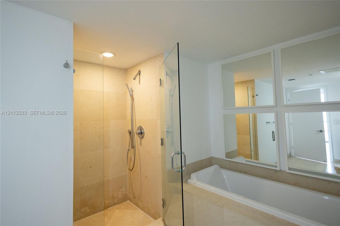 Walk-in shower with frameless glass enclosure, recessed ceiling lighting, wall-mounted handheld showerhead, built-in soaking tub, and square wall-mounted mirrors
