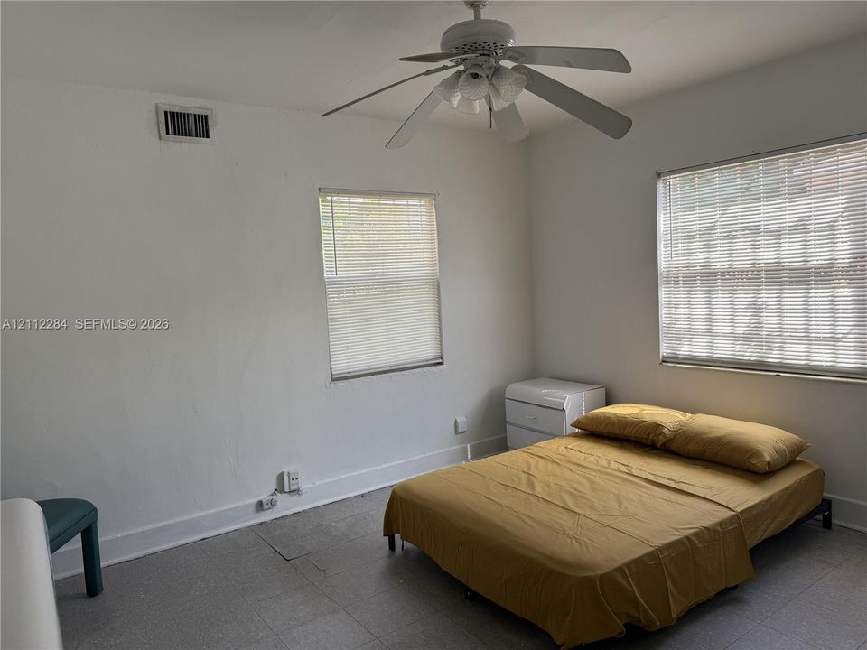 Bedroom featuring neutral wall paint, dual windows with integrated blinds, and a white ceiling-mounted fan with light fixture