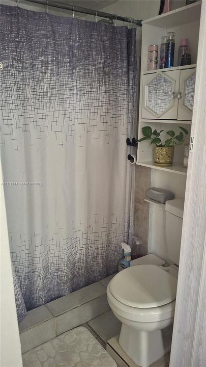 Built-in white cabinetry with dual storage compartments, ceramic tile tub surround, and standard-height commode