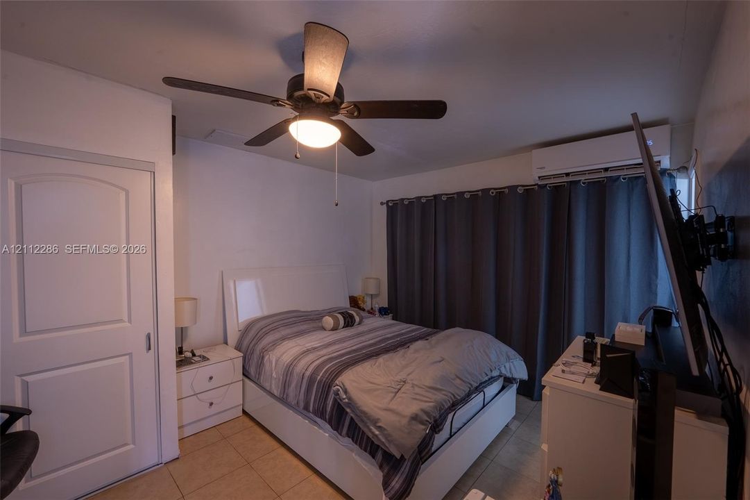 Room featuring tile flooring, a wall-mounted climate control unit, and a ceiling fan with integrated lighting