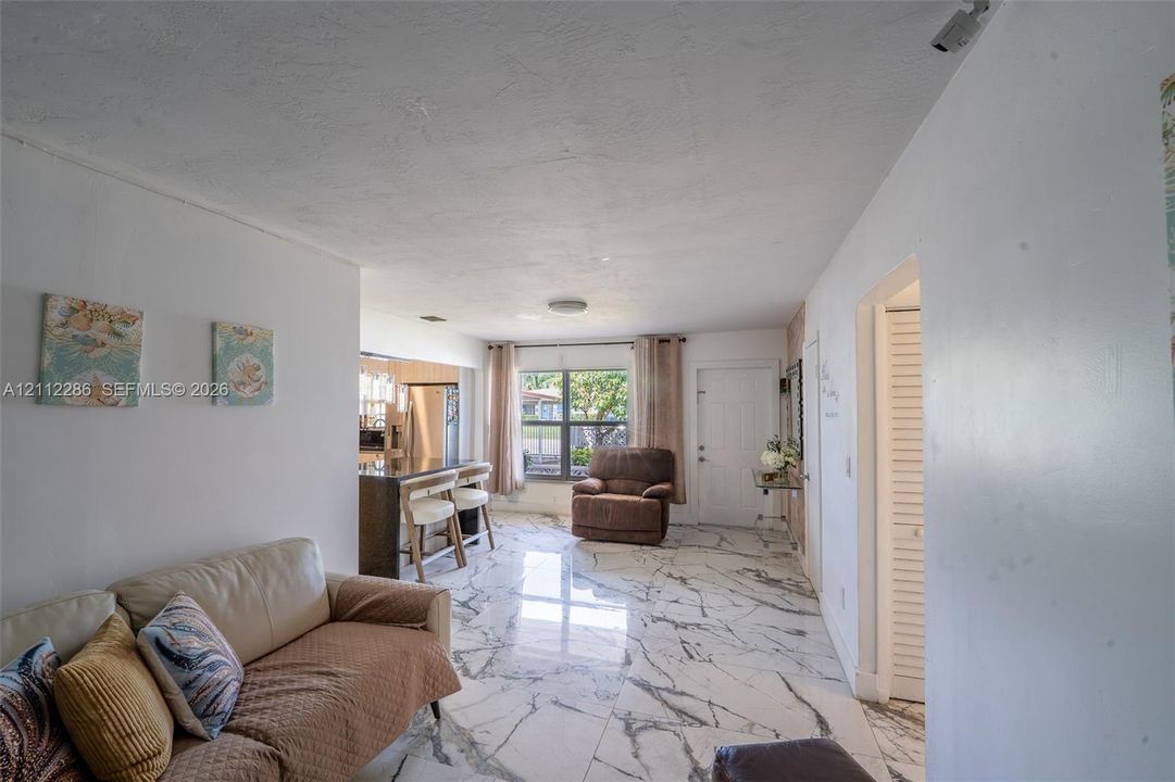 Large-format tile flooring with a neutral veined pattern, recessed ceiling lighting, and a kitchen island with a dark countertop
