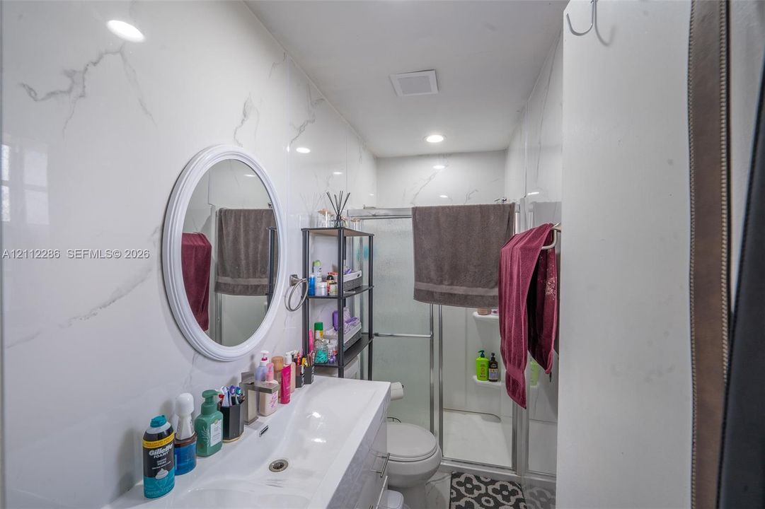 Bathroom featuring large-format wall tiles with a veined pattern, a single-basin integrated vanity, oval-framed mirror, and a walk-in shower with glass enclosure