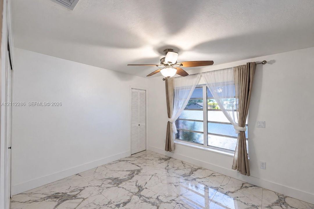 Large-format stone-style tile flooring featuring high-contrast veining, multi-blade ceiling fan with integrated lighting, and louvered closet doors
