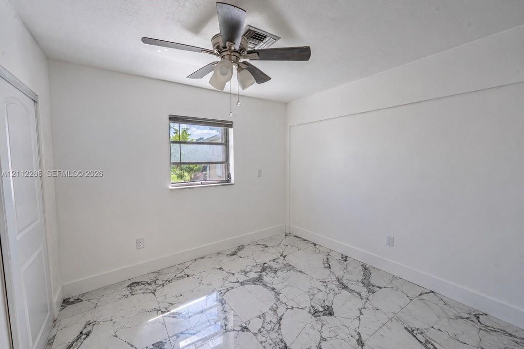Room featuring large-format stone-look tile flooring, a multi-blade ceiling fan with integrated lighting, and a single-pane window with horizontal blinds
