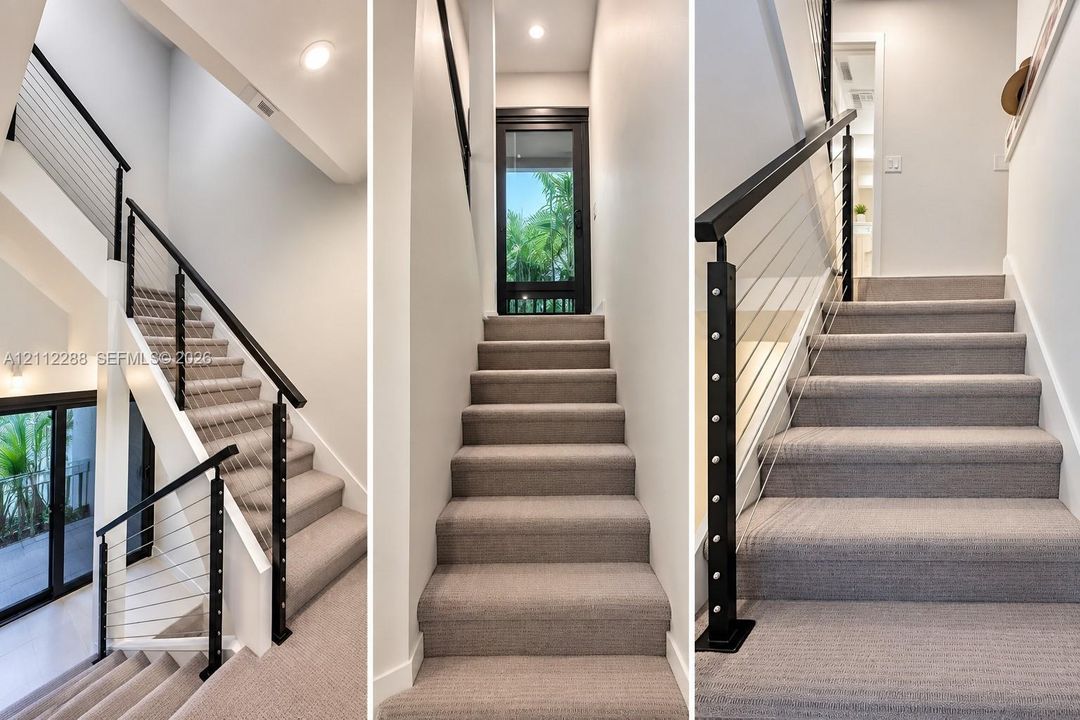 Staircase featuring neutral carpeted treads, a black metal handrail, horizontal cable railing system, and recessed ceiling lighting