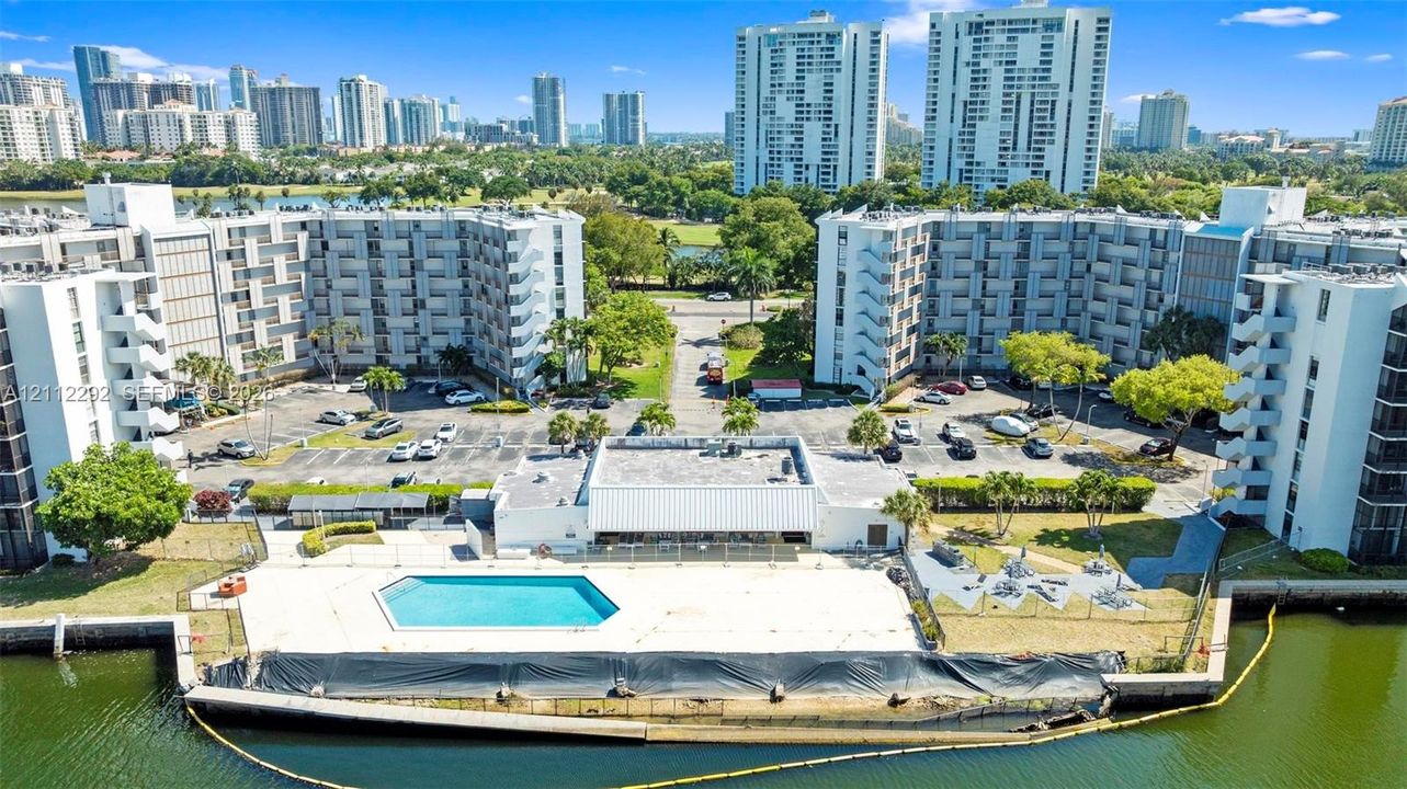Waterfront multi-story residential complex featuring an outdoor swimming pool, paved surface parking, and manicured perimeter landscaping