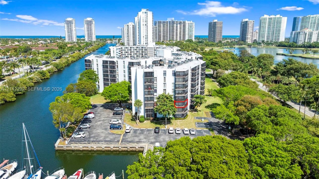 Multi-story waterfront condominium building featuring exterior balconies, paved surface parking, and a bulkhead-lined canal with boat slips