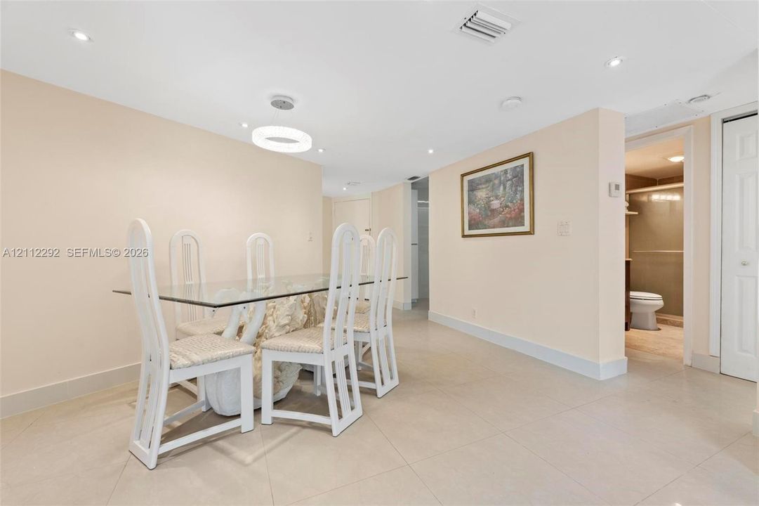 Open-concept area featuring light-toned tile flooring, recessed ceiling lighting, a modern circular LED pendant fixture, and a white paneled door