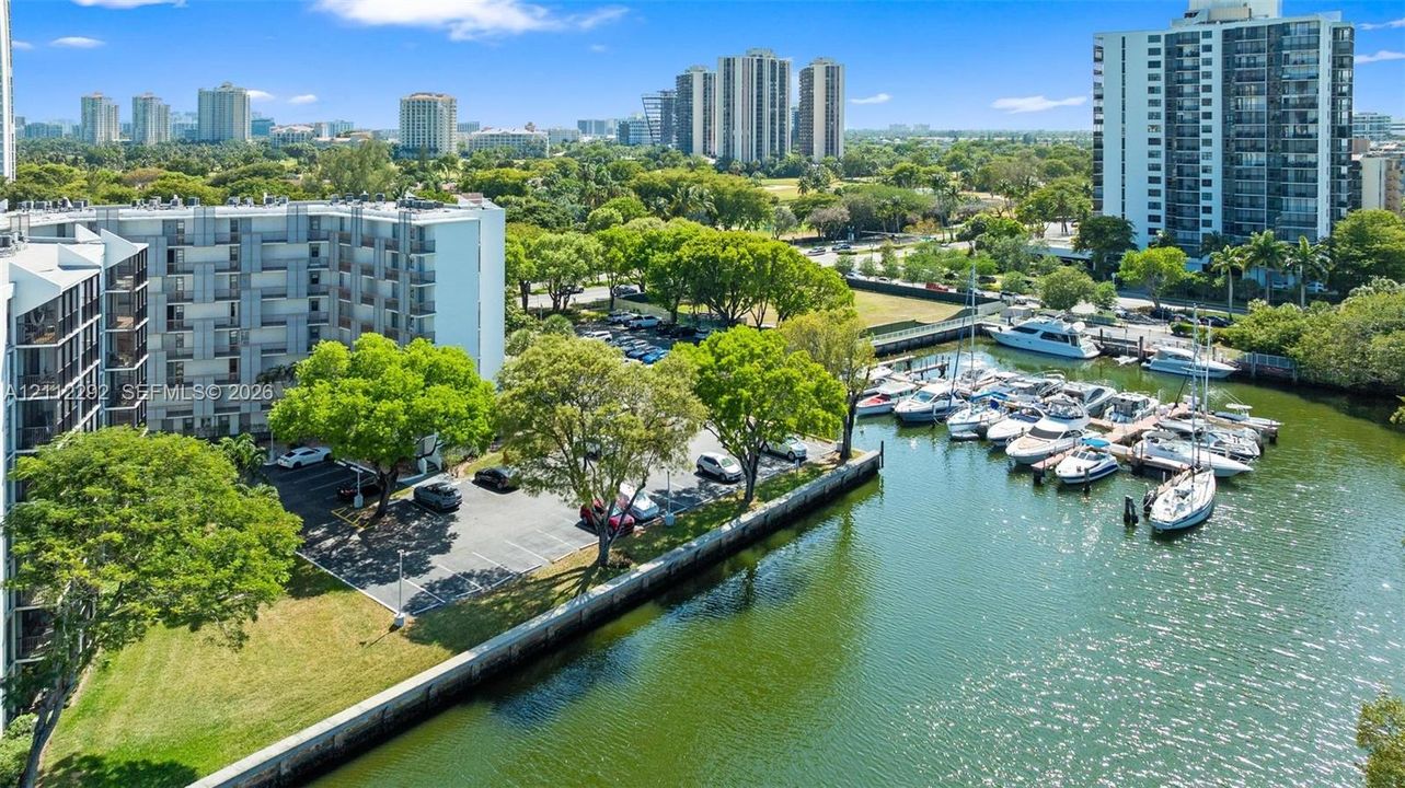 Aerial perspective of multi-story residential building featuring on-site parking, mature landscaping, paved bulkhead, and integrated boat slips