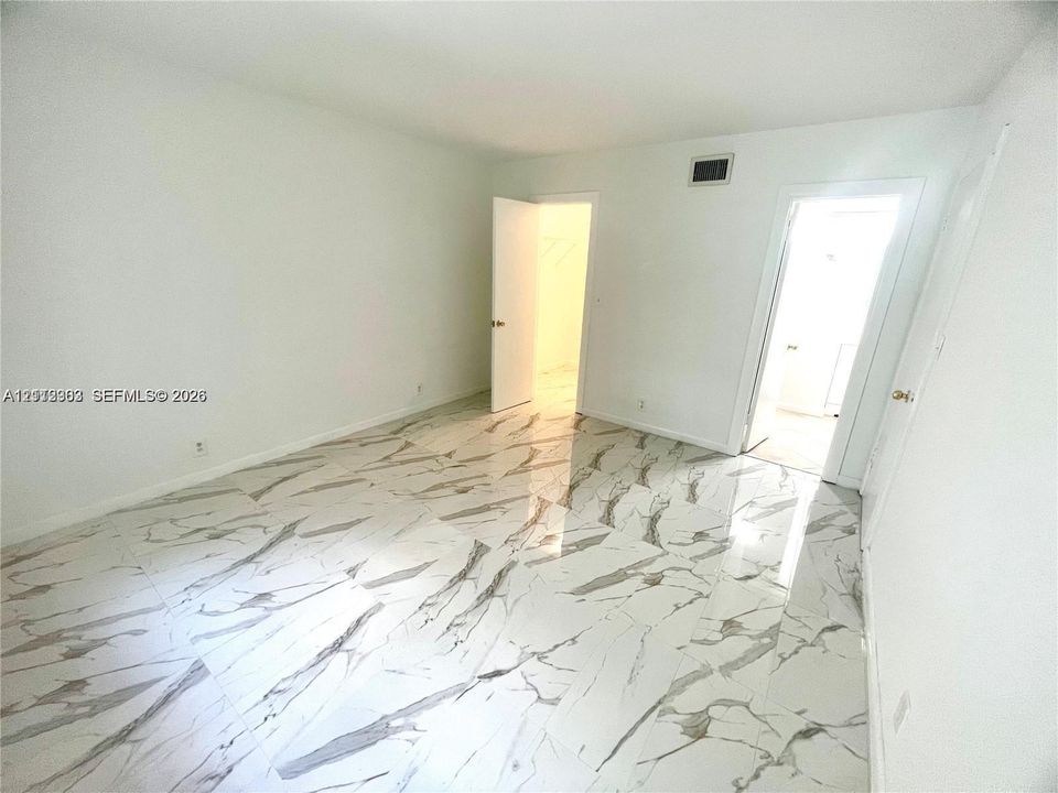 Large-format polished tile flooring featuring a decorative veined pattern, neutral wall finishes, and multiple interior doors