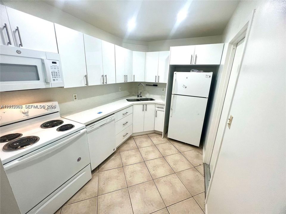 Kitchen featuring white cabinetry, solid-surface countertops, tile flooring, and integrated white appliances including a range, over-the-range microwave, and dishwasher