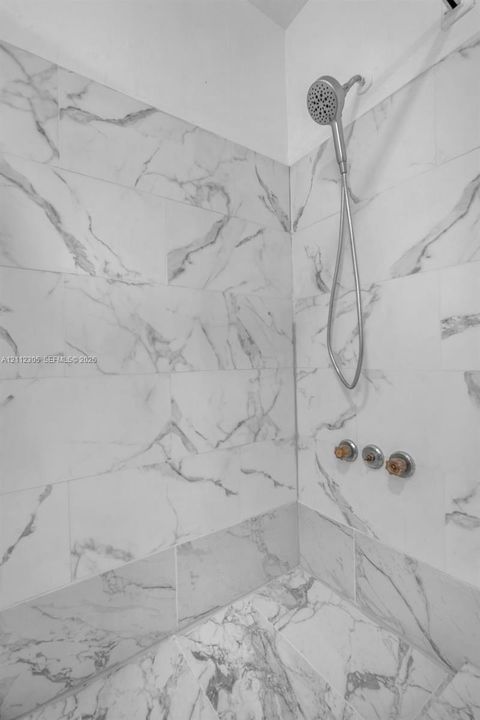 Shower enclosure featuring large-format veined tile surround, metallic handheld shower fixture, and circular multi-handle valve controls