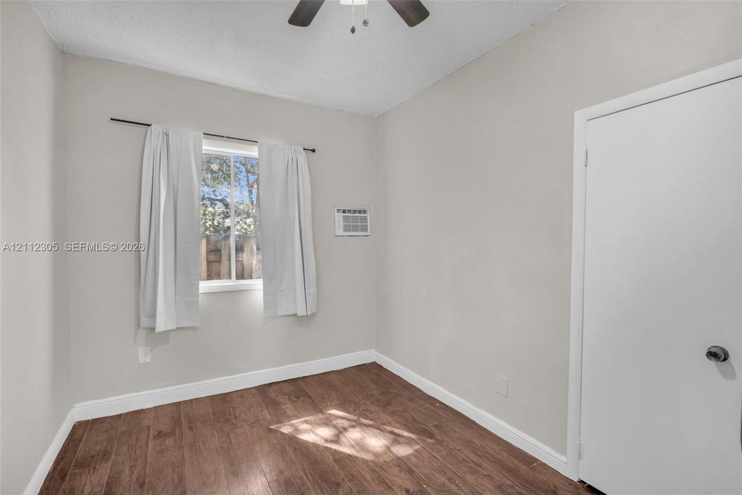 Interior room featuring wood-finish flooring, a ceiling fan, a window, and a built-in wall air conditioning unit