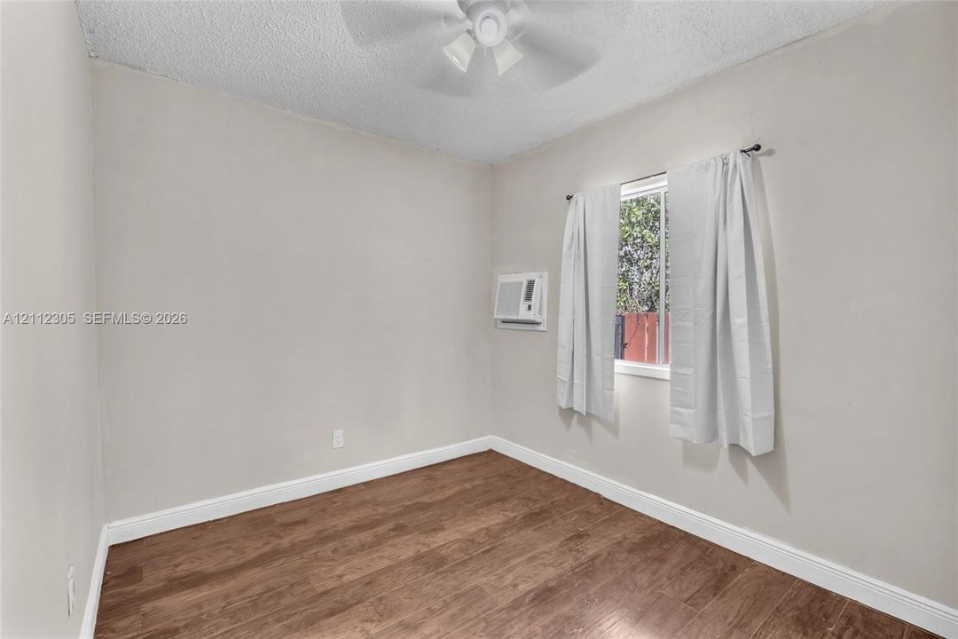 Room featuring wood-finish flooring, a ceiling fan, and a wall-mounted cooling unit