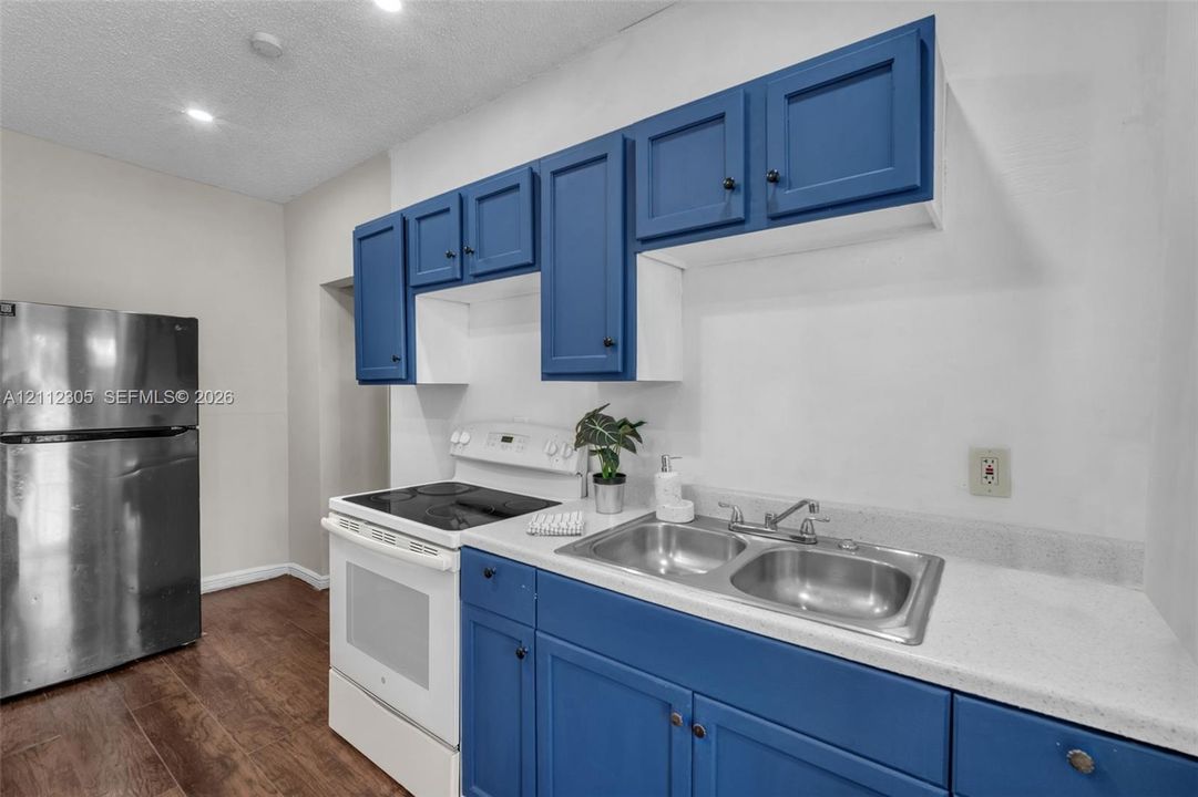 Kitchen featuring blue cabinetry, white countertops, double basin stainless steel sink, stainless steel refrigerator, and wood-finish flooring