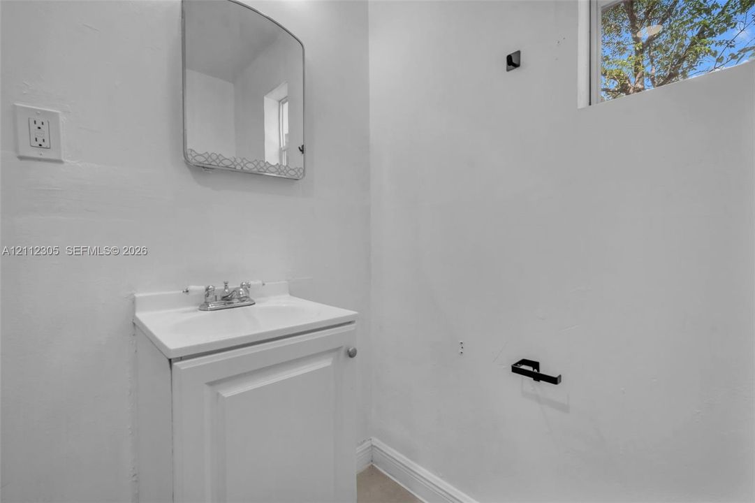 White vanity cabinet with an integrated top, chrome finish faucet, wall-mounted rectangular mirror, and matte black hardware fixtures