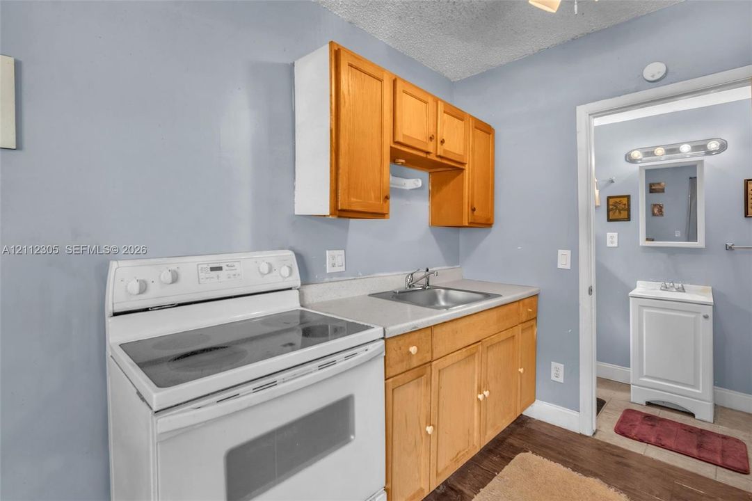 Kitchenette featuring wood cabinetry, a stainless steel sink, a white electric range, and wood-finish flooring, with a separate vanity area containing a white pedestal sink and wall-mounted light fixture