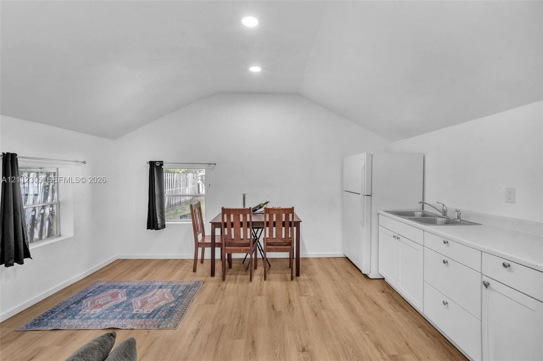 Vaulted ceilings, wood-finish flooring, recessed lighting, white cabinetry, and stainless-steel sink with a chrome faucet
