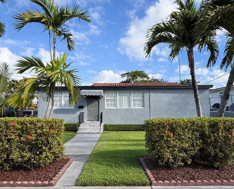 Single-story residence featuring a terracotta-tile roof, stucco exterior, concrete entryway steps with wrought-iron railings, and manicured landscaping