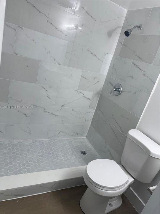 Shower enclosure featuring large-format veined wall tile, mosaic hexagonal floor tile, chrome plumbing fixtures, and a solid-surface threshold