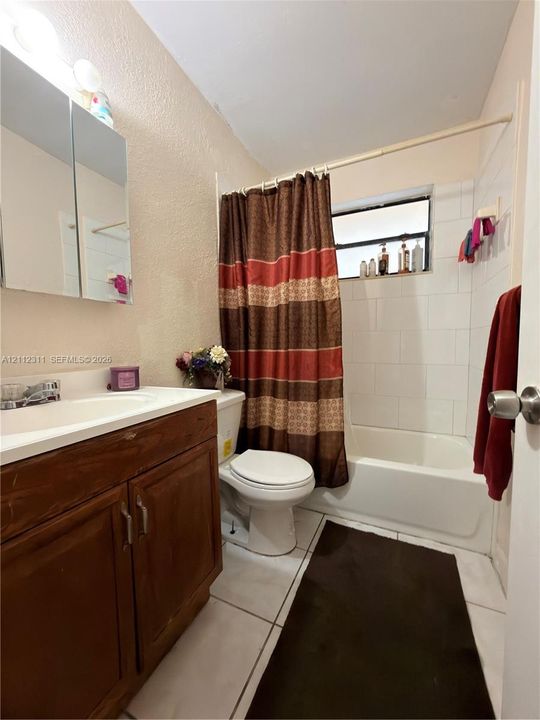 Full bathroom featuring a wood-finish vanity with an integrated sink, a mirrored medicine cabinet, and a tub-shower combination with white wall tile