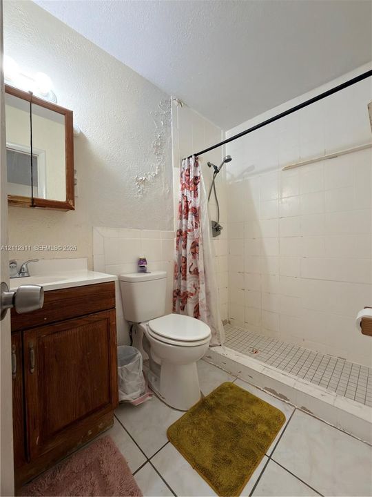 Bathroom featuring a wood-finish vanity with a single-basin sink, wall-mounted medicine cabinet, white tile wall surround, tile shower flooring, and ceramic floor tile