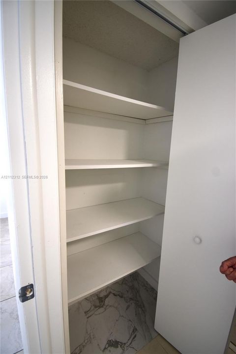 Built-in storage closet featuring multiple fixed white shelves and stone-patterned tile flooring