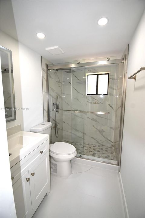 Bathroom featuring a white vanity, glass-enclosed shower with large-format wall tile, hexagonal floor tile, and recessed lighting