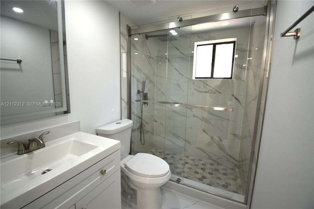 Bathroom featuring a vanity with an integrated sink, shower enclosure with sliding glass doors, stone-patterned tile wall surround, hexagonal floor tile, and wall-mounted mirror with integrated lighting