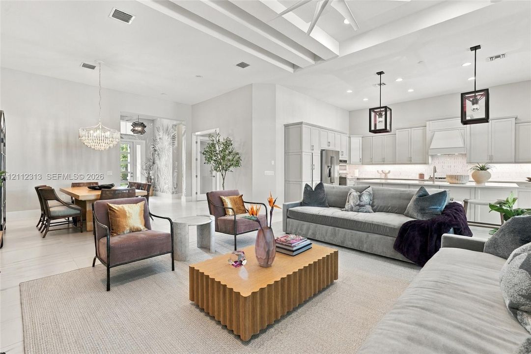 Open-concept living space featuring high tray ceilings, recessed lighting, neutral tile flooring, modern pendant light fixtures, and white cabinetry