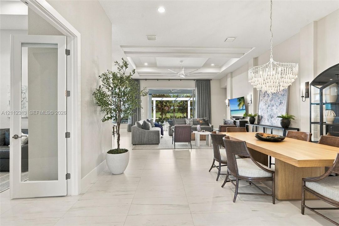 Open-concept interior featuring large-format tile flooring, tray ceilings with recessed lighting, and a crystal chandelier
