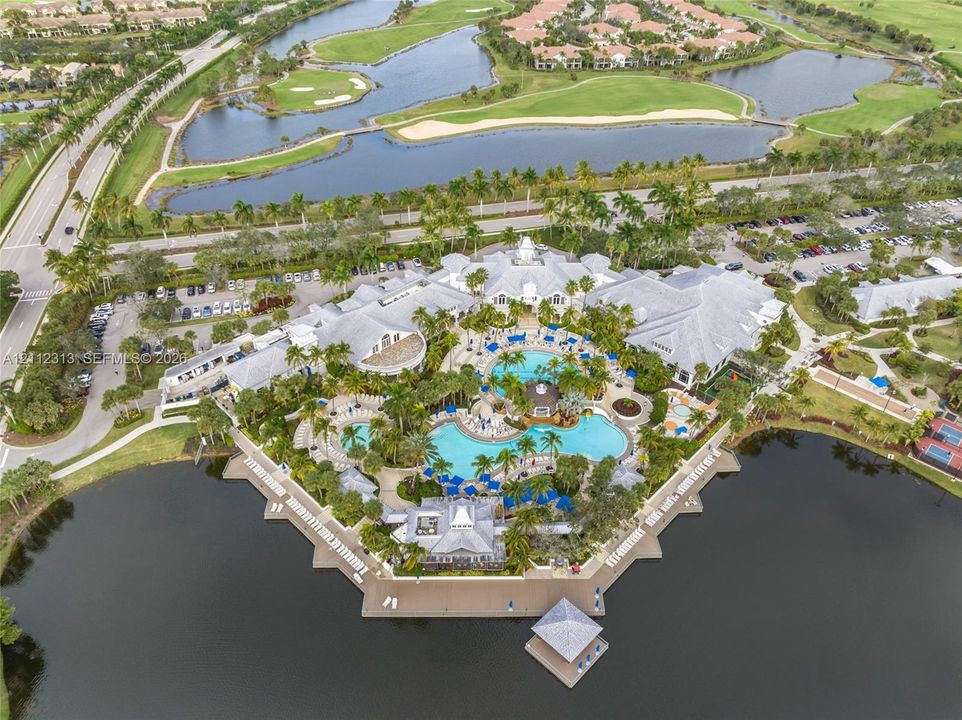 Aerial perspective of a multi-structure facility featuring a complex of resort-style swimming pools, expansive paved sun decks, a waterfront gazebo, and mature landscaping situated along a large lake