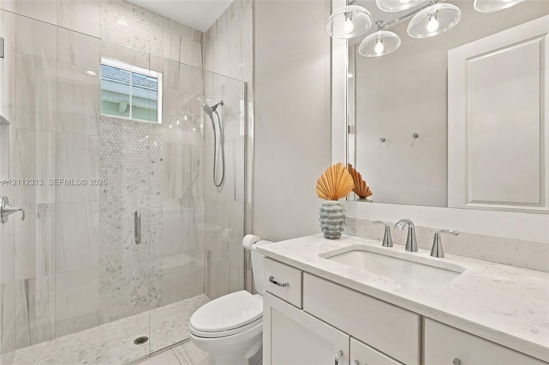 Bathroom featuring a vanity with a white countertop and undermount sink, a walk-in shower with a glass enclosure, floor-to-ceiling tilework, and a multi-bulb light fixture