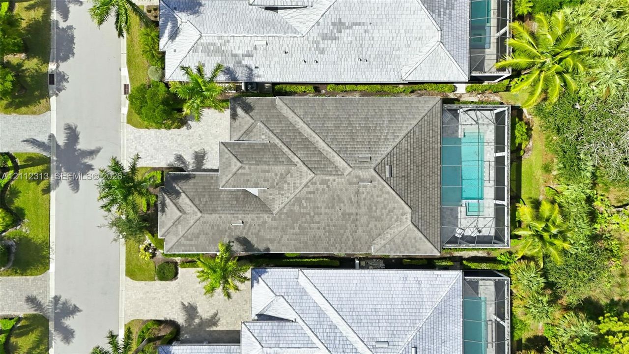 Aerial perspective featuring a multi-hipped roofline, paved driveway, and a screened-in pool enclosure