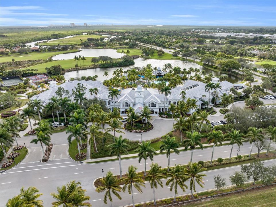 Aerial perspective of a multi-winged facility featuring a central clock tower, expansive pond frontage, mature palm tree landscaping, and paved circular drive