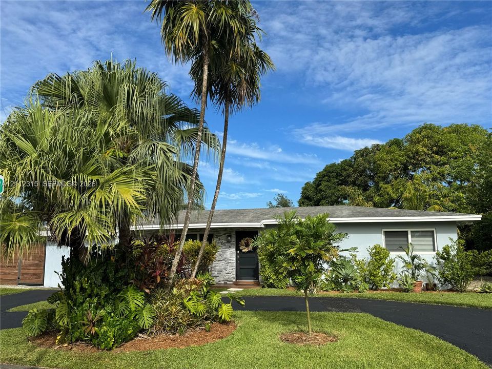 Single-story exterior featuring light-toned horizontal siding, a stone veneer facade, an asphalt driveway, and mature palm trees