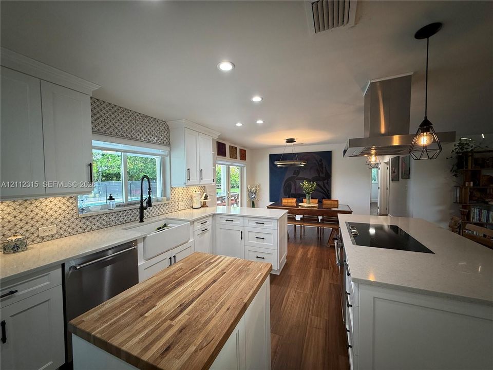 Kitchen featuring white shaker-style cabinetry, quartz countertops, a butcher block island top, a farmhouse sink, and a stainless steel range hood
