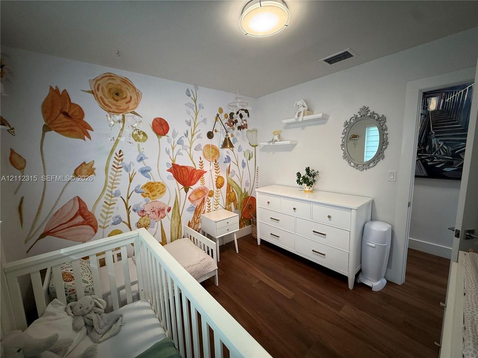 Interior space featuring wood-finish flooring, a floral-patterned accent wall, two built-in wall shelves, and a circular wall-mounted mirror