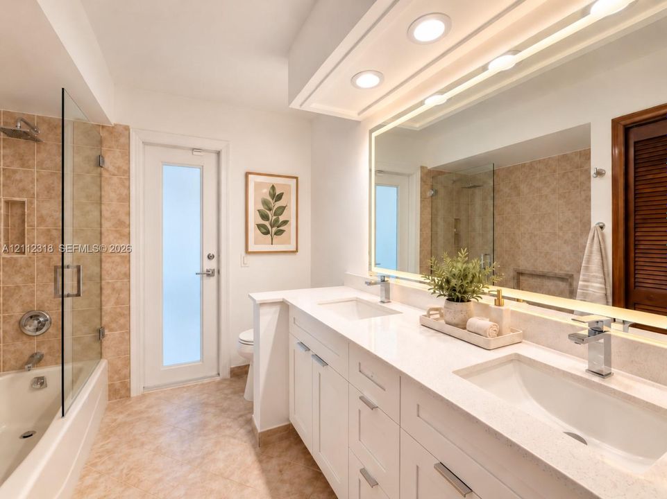 Double vanity featuring white cabinetry, integrated stone-finish countertops, dual undermount sinks, and a full-width LED-backlit mirror