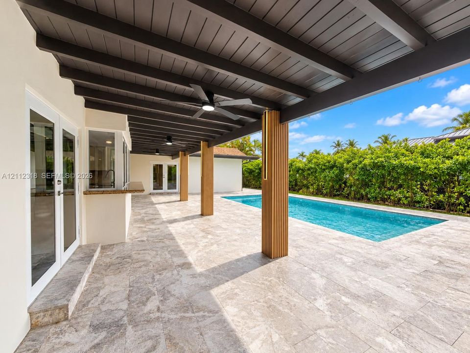 Covered patio featuring an exposed-beam ceiling, ceiling fans, stone-finish flooring, built-in counter, and a rectangular swimming pool