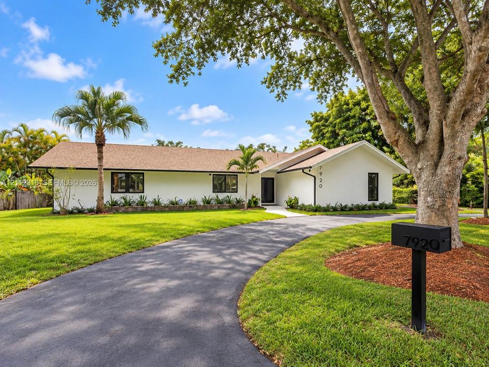 Single-story exterior featuring white stucco siding, a shingled roof, dark-framed windows, and an asphalt driveway set within a manicured lawn