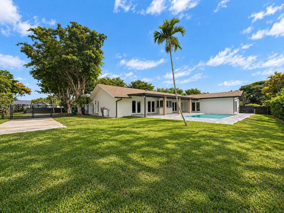 Expansive backyard featuring a sprawling lawn, in-ground swimming pool, stone-paver patio, covered porch, and mature landscaping