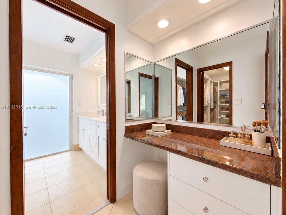 Stone-topped vanity with built-in cabinetry, large wall-mounted mirror, recessed lighting, and tile flooring