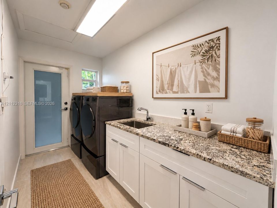Laundry room featuring white shaker cabinetry, stone-finish countertops, an integrated stainless steel basin, and a door with frosted glass insert