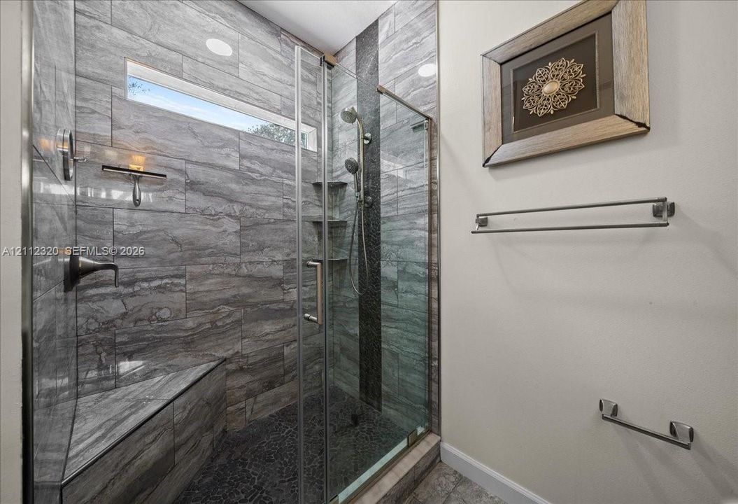 Walk-in shower featuring large-format stone-tile walls, built-in corner bench, glass enclosure, and multi-setting shower head