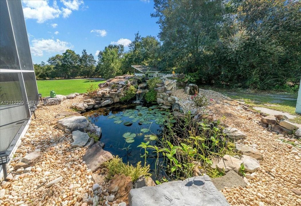 Custom stone water feature with built-in rock fountain, pebble landscaping, and aquatic plants